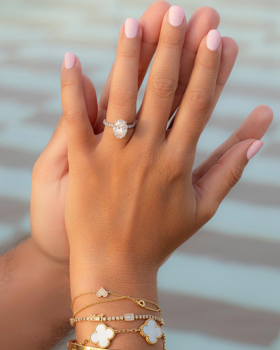 Close-up of an oval engagement ring and stacked gold bracelets