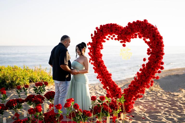 Couple holding hands in front of the rose heart, the sea behind them